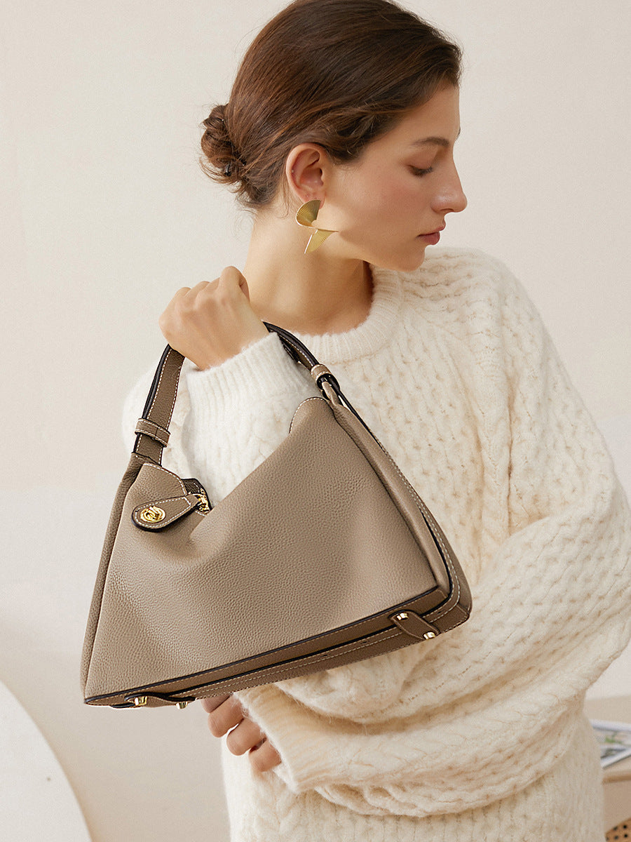 Woman carrying the taupe grained leather hobo bag by its top handle with a cream cable knit sweater