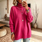 Woman in a rose red turtleneck knit sweater with a folded high collar and ribbed cuffs, jeans below