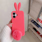 Deep pink rabbit ear silicone iPhone case held in hand with plush pom pom tail