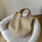 Paper straw bag resting on a white boucle chair, showing the two tan leather look shoulder straps