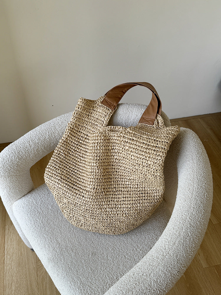 Paper straw bag resting on a white boucle chair, showing the two tan leather look shoulder straps