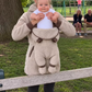 Beige teddy fleece hoodie with a baby lifted from the front pouch, shown in a park