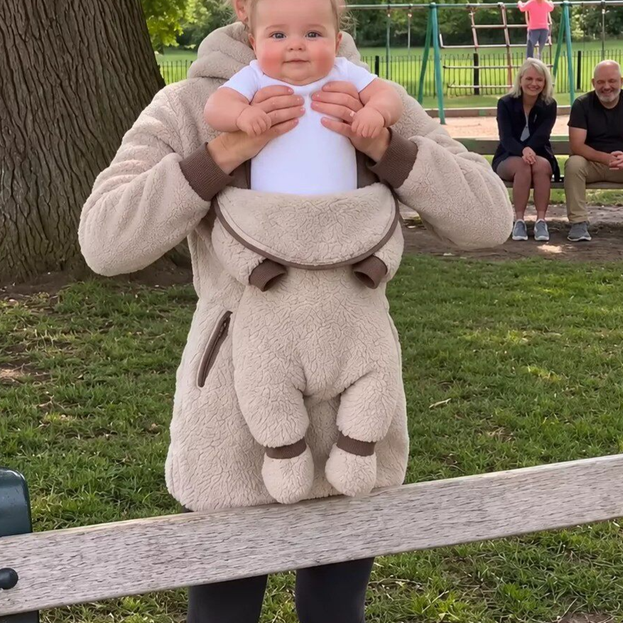 Beige teddy fleece hoodie with a baby lifted from the front pouch, shown in a park