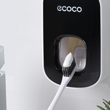 Black wall mounted toothpaste dispenser with a toothbrush pressed up into the pad at the base