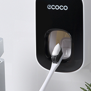 Black wall mounted toothpaste dispenser with a toothbrush pressed up into the pad at the base