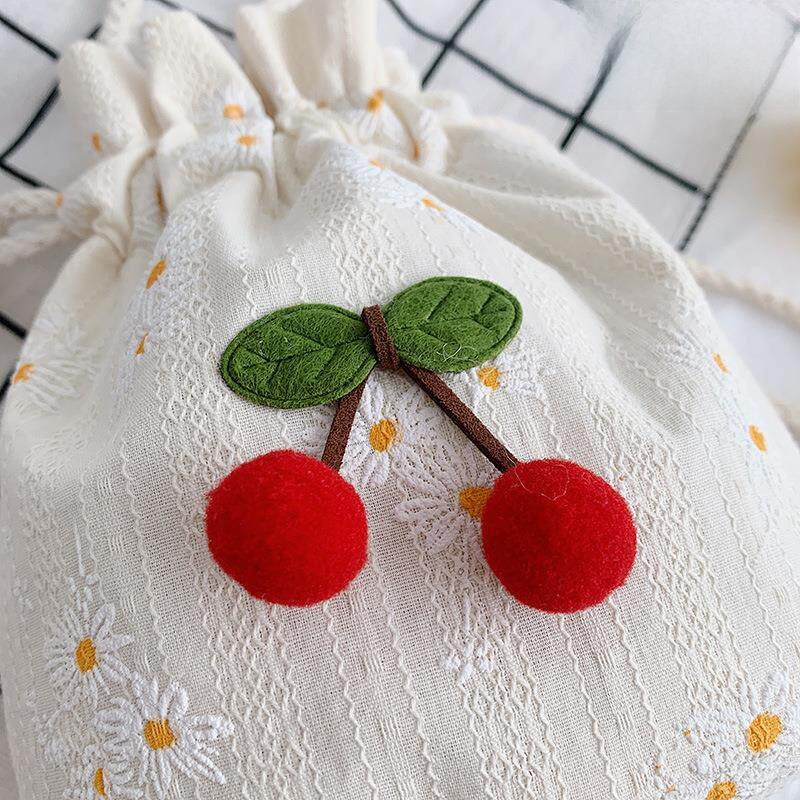 Close up of red pom pom cherry charm and green felt leaves on daisy canvas bag