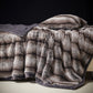 Taupe Gray option: silver gray vegan fur blanket with dark tipped pile and a gray border draped over a bed