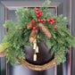 Christmas wreath held against a dark door, with evergreen sprigs, pine cones, red berries and a cluster of gold-tone bells