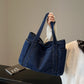 Dark blue denim shoulder tote held by its twin straps, roomy body with a top opening and side pockets