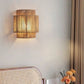 Lit hemp rope wall lamp with stacked tiers on a white wall above a cane chair back and orange flowers