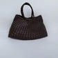Dark brown woven PU handbag, front view with two braided top handles on a pale backdrop