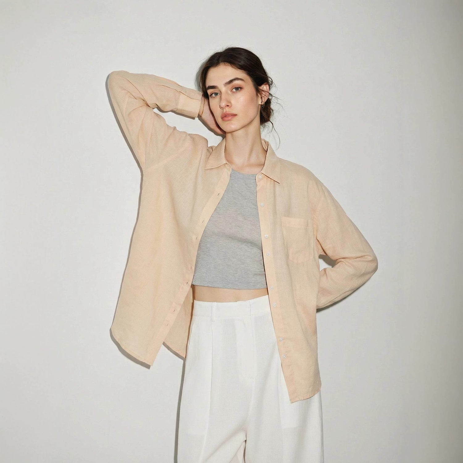 Woman wearing a semi sheer linen button-up shirt layered open over a fitted tank top