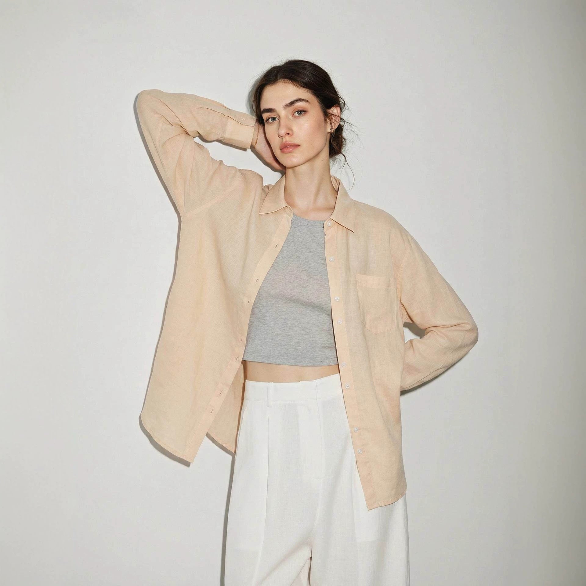 Woman wearing a semi sheer linen button-up shirt layered open over a fitted tank top