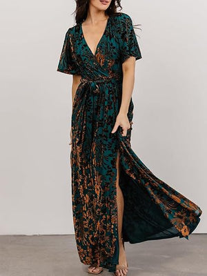 Woman in a teal and copper floral burnout velvet maxi dress with a deep V neck holding the side slit