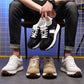 Man seated holding black sneakers with cream, tan, and gray pairs on the floor