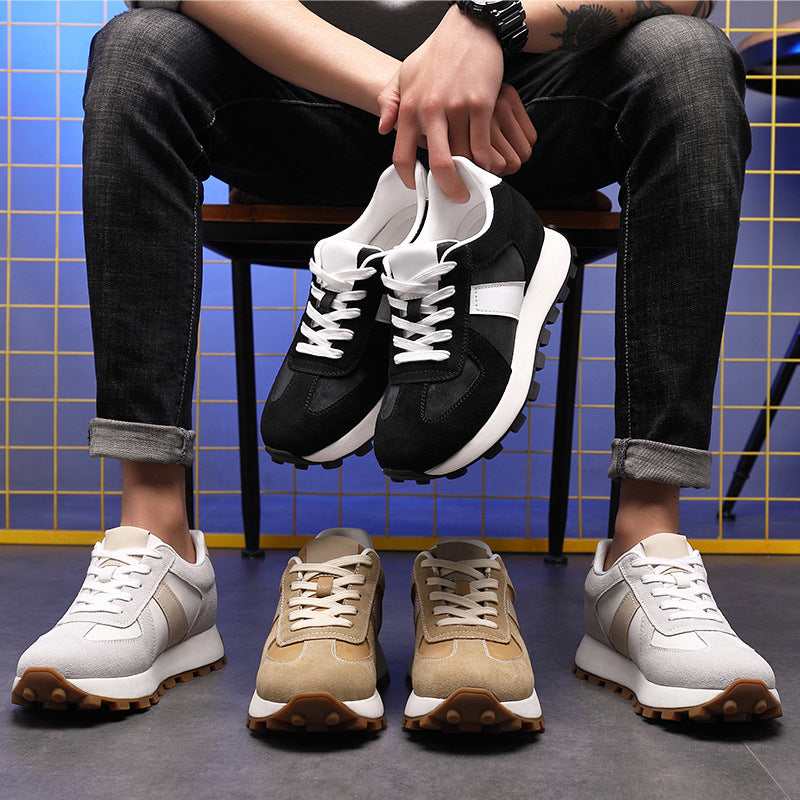 Man seated holding black sneakers with cream, tan, and gray pairs on the floor