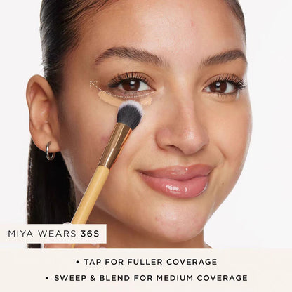 Woman with a bamboo handled concealer brush applying concealer under her eye, with tap and sweep coverage captions