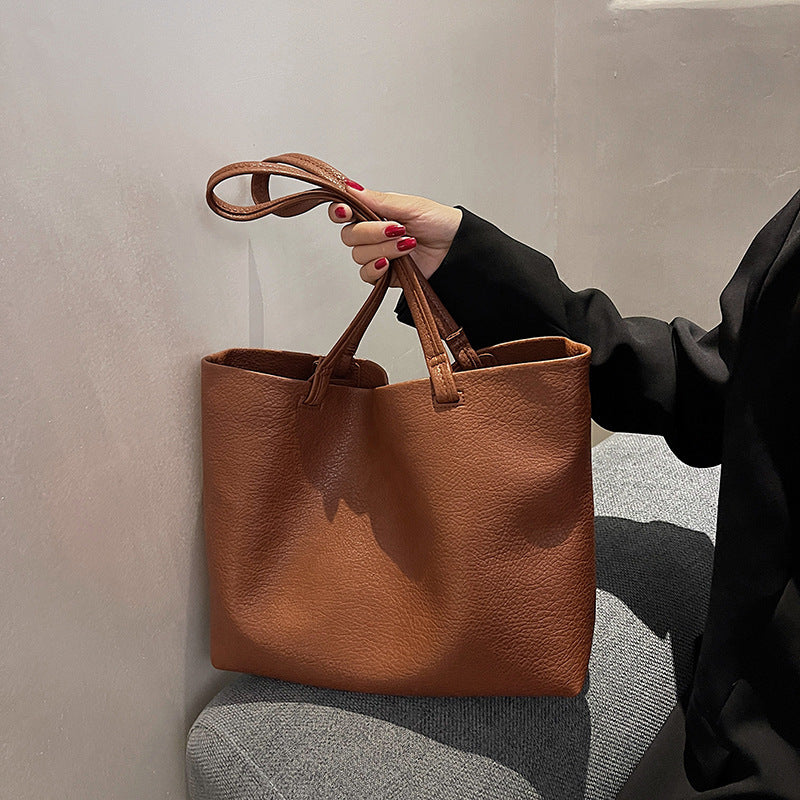 Hand holding the straps of a tan PU tote bag against a gray seat, Brown option photo