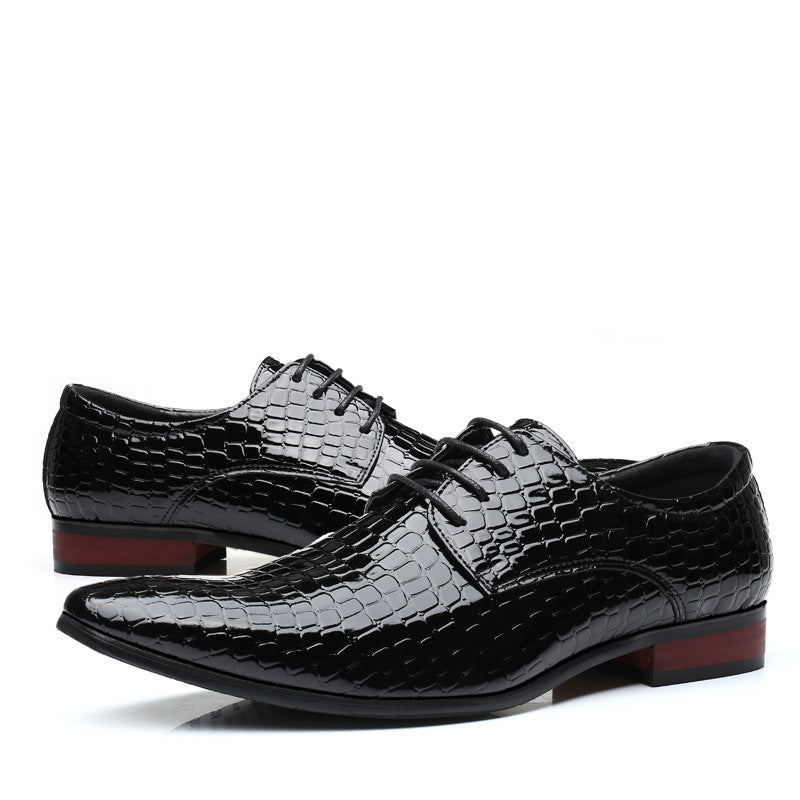 Pair of black crocodile embossed pointed toe derby dress shoes with a red brown heel, side view on white