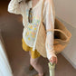 Back and side of loose ivory floral tee worn with woven bag and yellow shorts