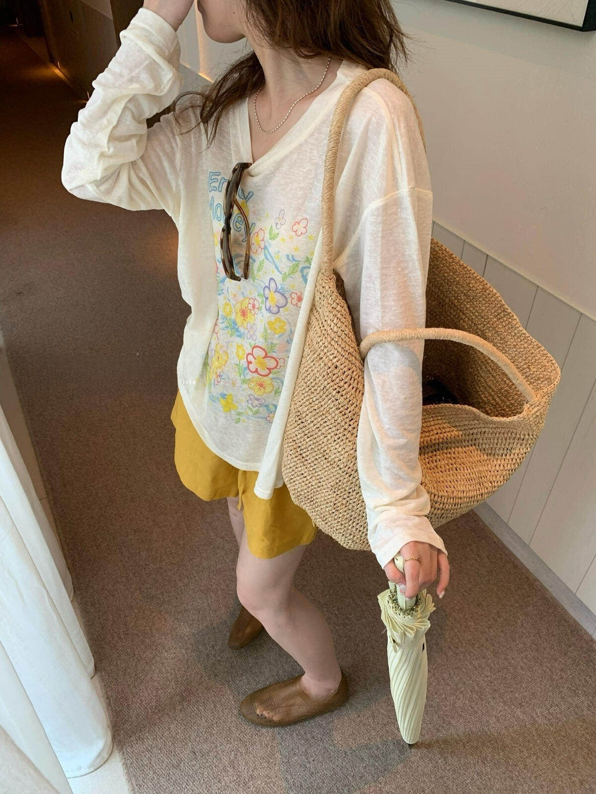 Back and side of loose ivory floral tee worn with woven bag and yellow shorts