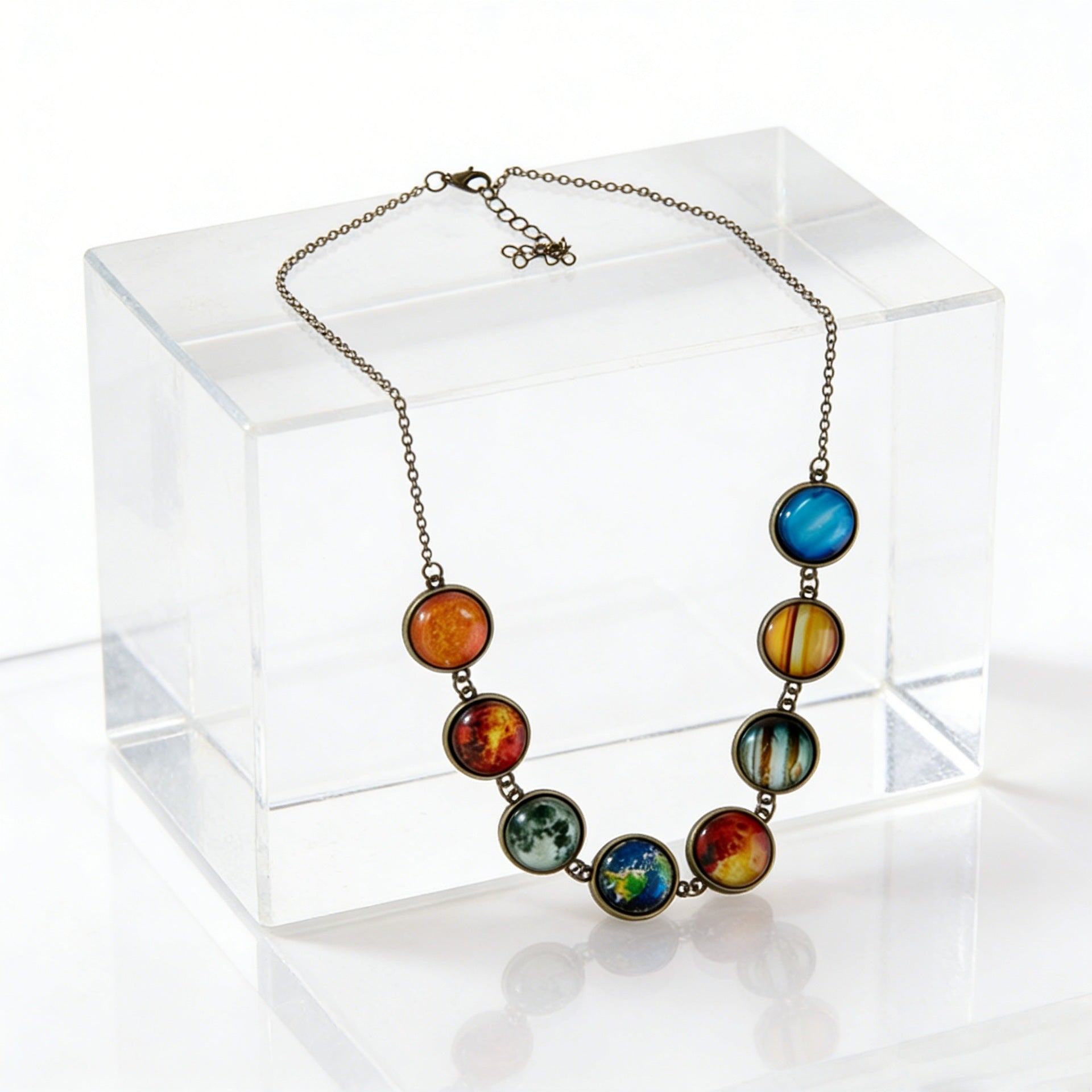 Solar system cabochon necklace draped over a clear acrylic block, lobster clasp and extender chain visible