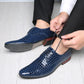 Man tying the laces of a navy blue crocodile embossed derby shoe, the other shoe showing a printed text sole