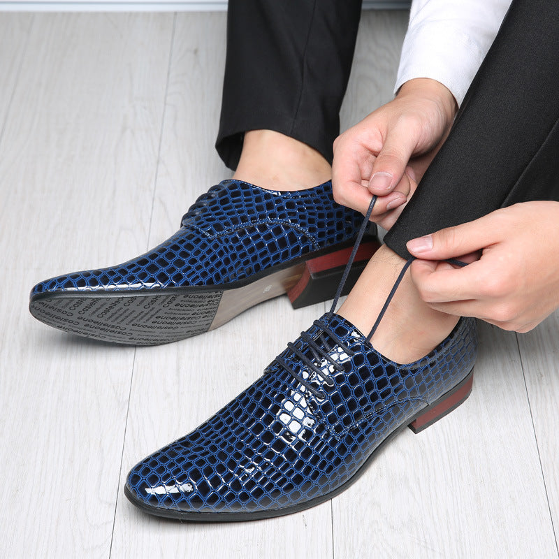 Man tying the laces of a navy blue crocodile embossed derby shoe, the other shoe showing a printed text sole