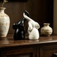 Matte black and white couple elephant figurines with trunks meeting, on a wooden dresser with vases