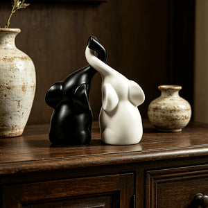 Matte black and white couple elephant figurines with trunks meeting, on a wooden dresser with vases