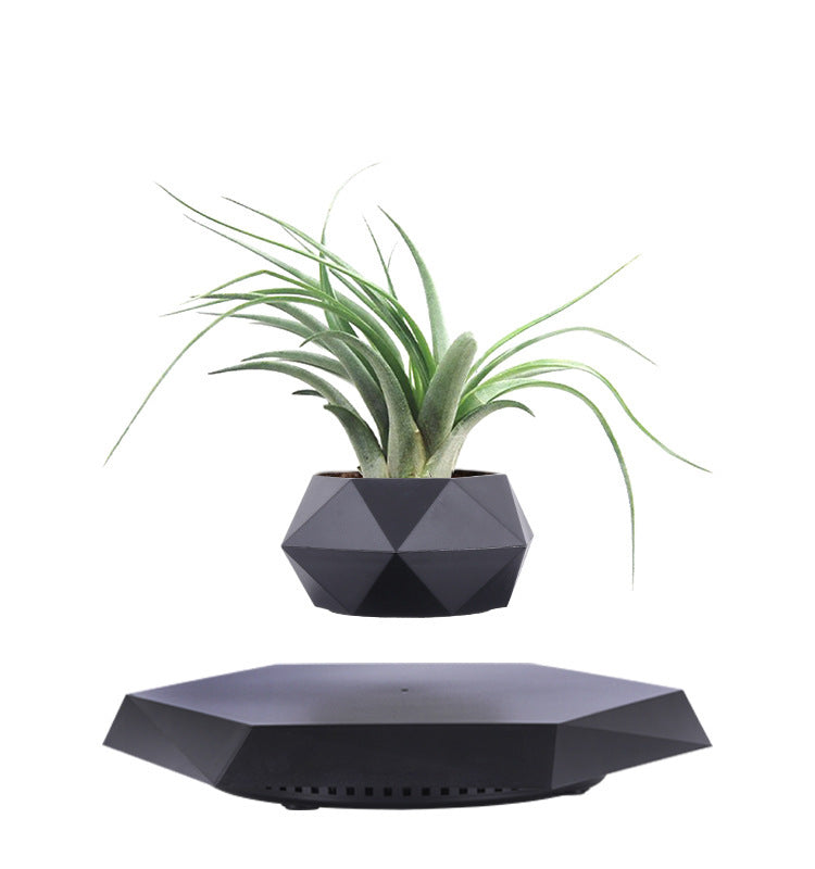 Magnetic levitation planter in matte black with a green artificial plant, on a desk