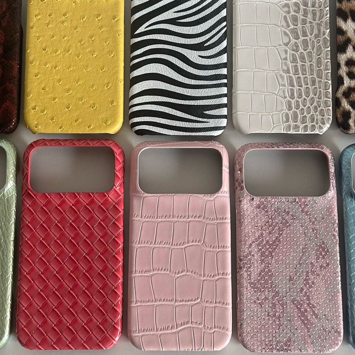 Assorted half-cover phone cases in yellow ostrich, zebra, white crocodile, leopard, woven red and pink prints on grey