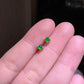 Two green cabochon studs held between fingers, domes polished smooth in silver tone prongs
