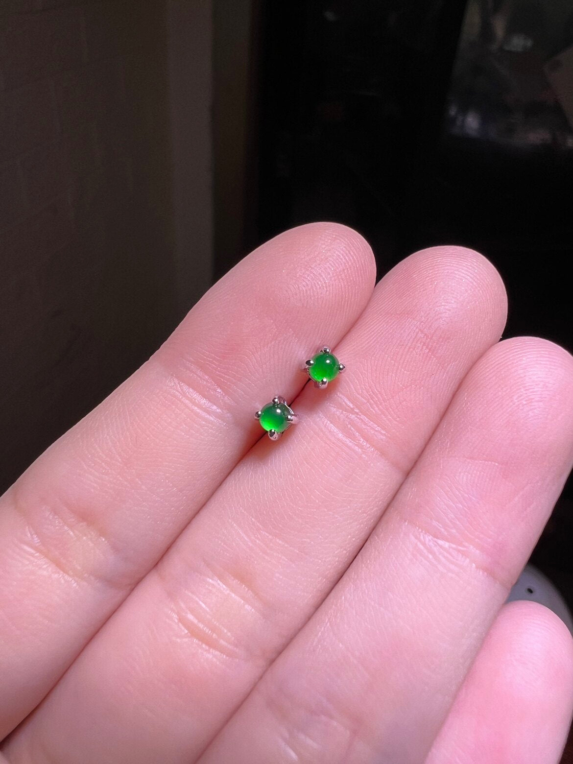 Two green cabochon studs held between fingers, domes polished smooth in silver tone prongs