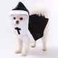 White fluffy dog wearing a black cape nun costume with white hood trim and a black cross front panel