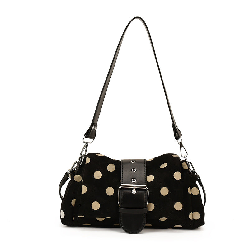 Black polka dot shoulder bag with cream dots and wide buckle band hanging from its shoulder strap on white