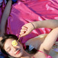 Woman lying on hot pink slip silk with a flower held over one eye