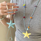 Blue and yellow resin starfish cord necklaces shown held and worn over a grey top