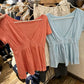 Orange and light blue short-sleeve V-neck tops with gathered hems on a store rail