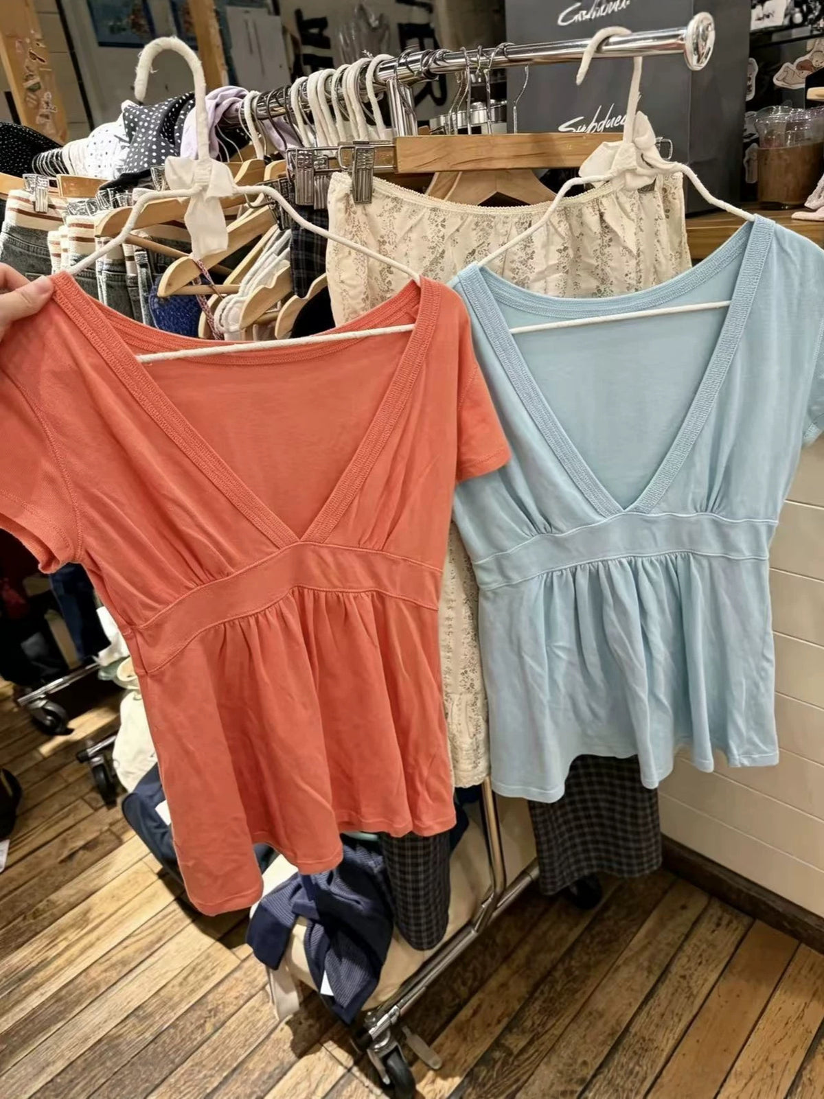 Orange and light blue short-sleeve V-neck tops with gathered hems on a store rail