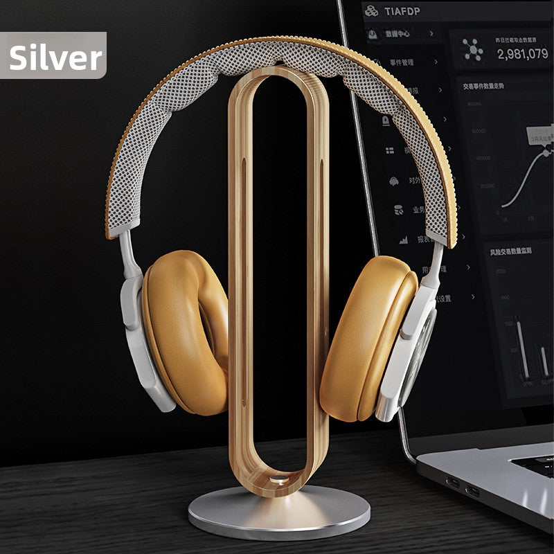 Silver wood grain headphone stand with over ear headphones beside a laptop on a dark desk