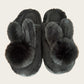 Black plush bunny slippers with two ears and a pom pom each, top view on a beige background, black variant