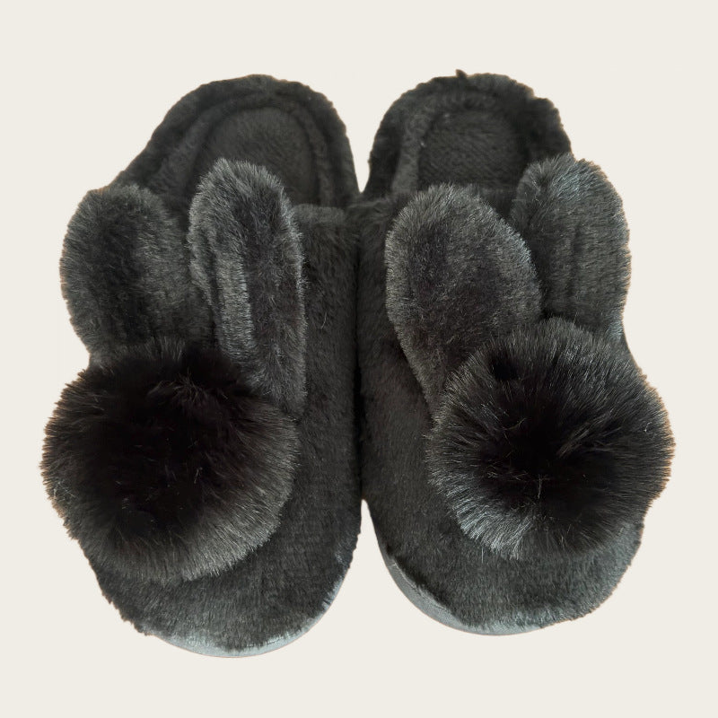 Black plush bunny slippers with two ears and a pom pom each, top view on a beige background, black variant