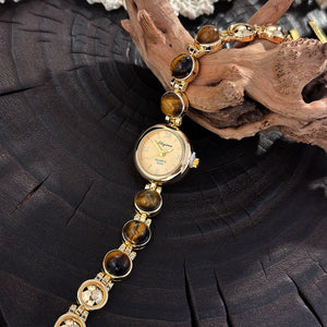 Tiger eye beaded bracelet watch with a small gold dial and Roman numerals held in hand