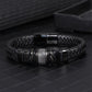 Mens black leather bracelet on a dark tiled surface beside a jewelry tray