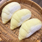 Creamy durian squishy option, pale matte segment pressed between fingers in a rattan tray