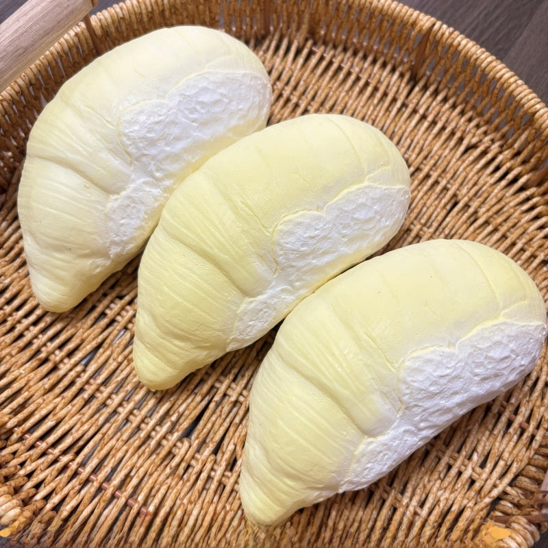 Creamy durian squishy option, pale matte segment pressed between fingers in a rattan tray