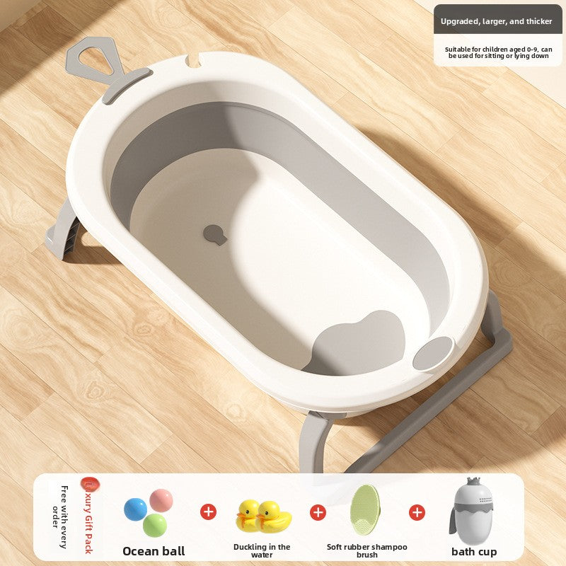 Cream and gray foldable baby bathtub on a wooden floor with a gift pack of balls, duck, brush and cup