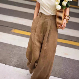 Coffee brown cotton linen high waist wide leg trousers worn with a woven straw bag on a street