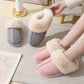 Gray and pink plush cuff mule slippers on a rug, one pair held open by a hand